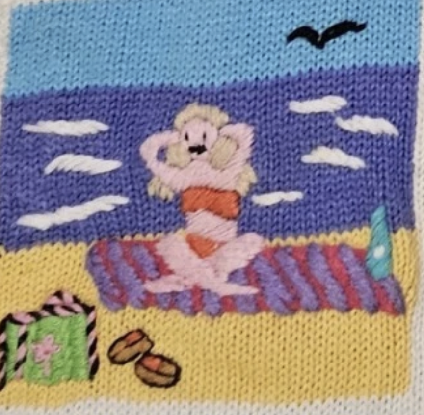 close-up of an applique of a woman sitting on a beach towel with her arms raised