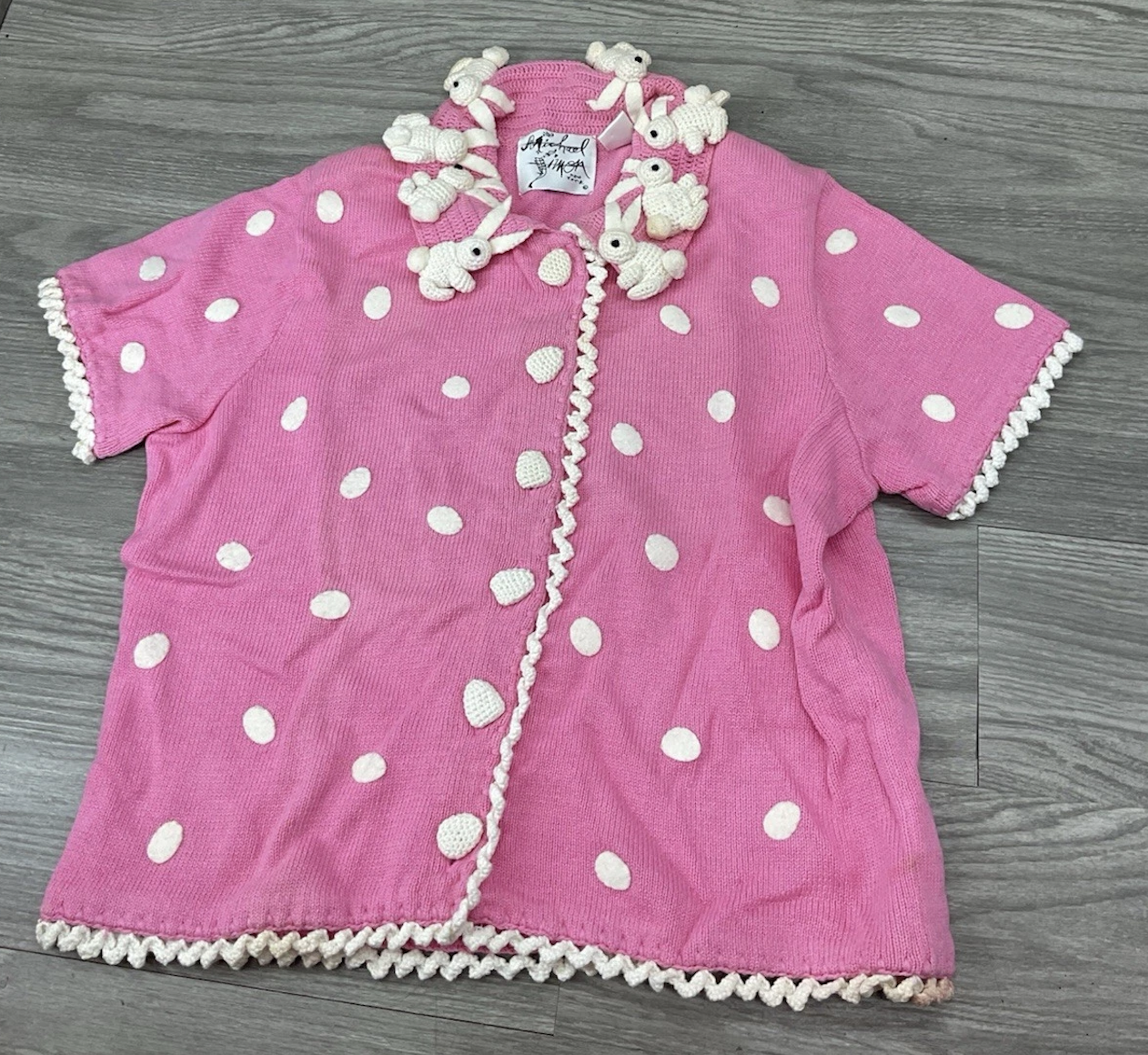 pink short-sleeved cardigan with white dots and three-dimensional crocheted white rabbits around teh collar