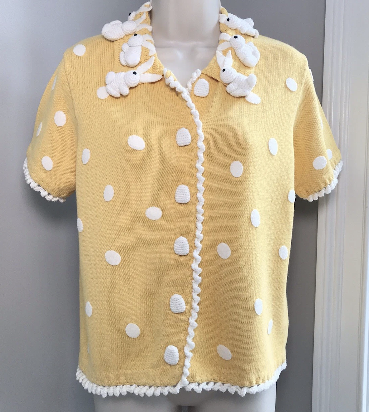 yellow short-sleeved cardigan with white dots and three-dimensional crocheted white rabbits around teh collar